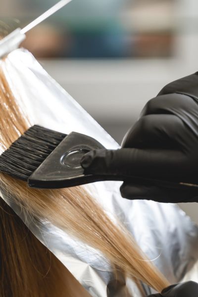 Close up of female hand using a brush while coloring hair in salon.
